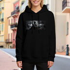 Outdoor photograph of a model in a women's hoodie bearing an armored figure in a smoky grayscale panel with lettering