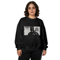 A monochrome cowl portrait layered over a newspaper-style panel printed on a women's crewneck sweatshirt, shown in a front model photo