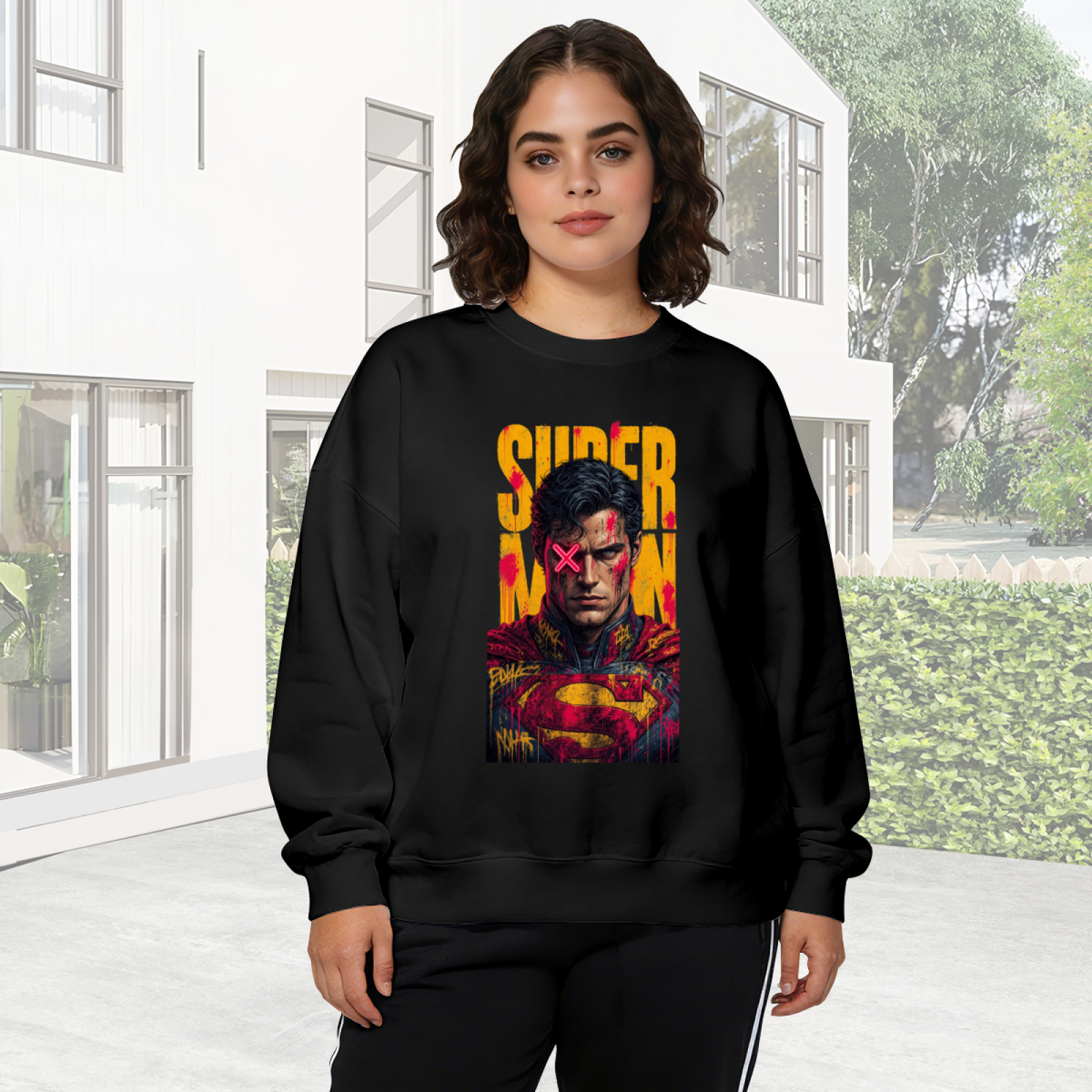 Outdoor photograph of a model in a women's crewneck sweatshirt bearing a tall caped graffiti portrait with a pink X across the eyes