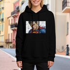 Lifestyle image outdoors: women's hoodie with a front graphic of a tightly cropped intense face above a cape against newsprint