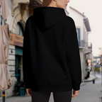 Outdoor view from behind of a model wearing the women's A Trident-Bearing Wanderer hoodie with its plain rear visible