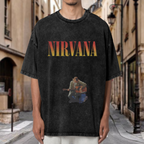 Nirvana Kurt Cobain Acoustic Washed Tee in Black, product image showing kurt Cobain seated with an acoustic guitar, with a Nirvana logo above the performance image.
