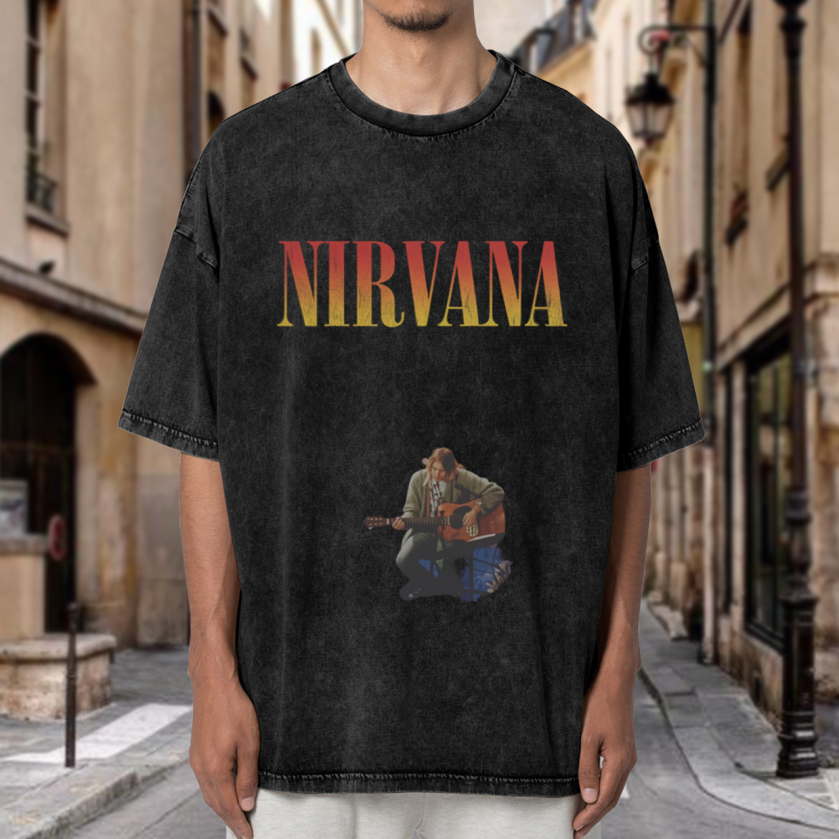 Nirvana Kurt Cobain Acoustic Washed Tee in Black, product image showing kurt Cobain seated with an acoustic guitar, with a Nirvana logo above the performance image.