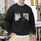 Men's crewneck sweatshirt worn outside, with the camera facing the graphic of a monochrome cowl portrait layered over a newspaper-style panel
